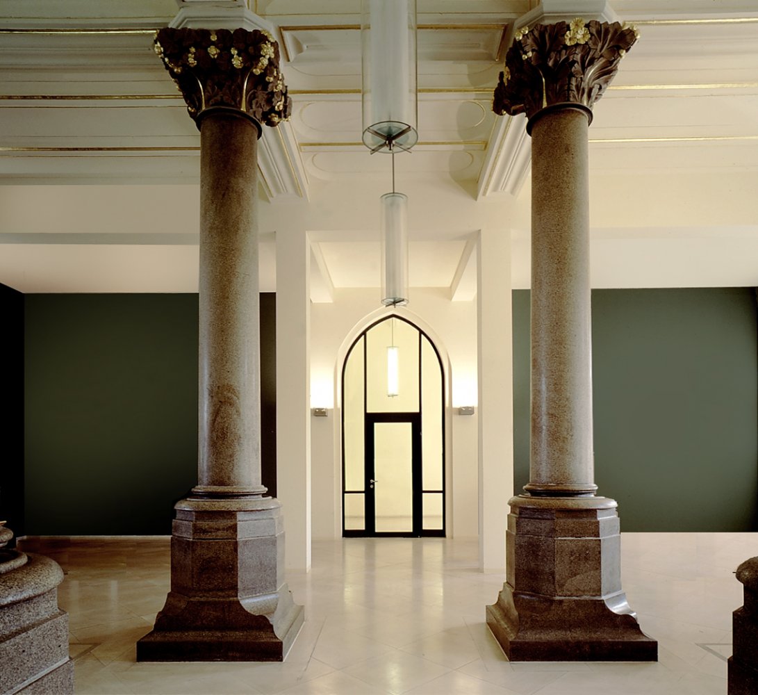 Kundenhalle mit hoher Deckenhöhe, grünen Wänden und altertümlichen Marmorsäulen. Blick auf die gläserne Tür zum Eingangsbereich.